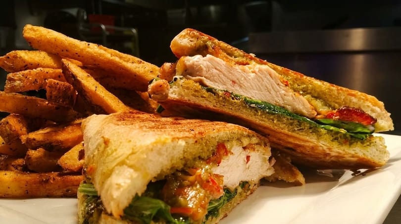 Grilled chicken panini with pesto, roasted red peppers, and spinach, served with seasoned fries.